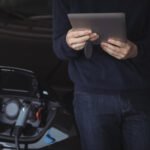 Mid Section Man Using Digital Tablet While Charging Electric Car 150x150